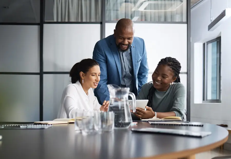 Executive leaning over a conference table to talk with two colleagues