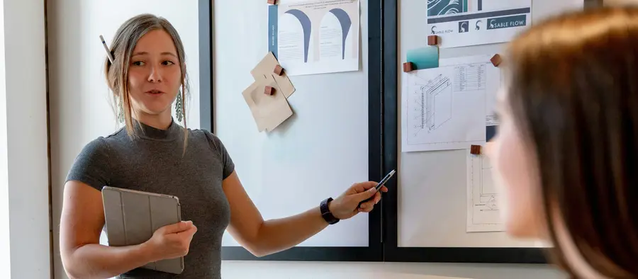 Team member presenting plans pinned to a board in a meeting