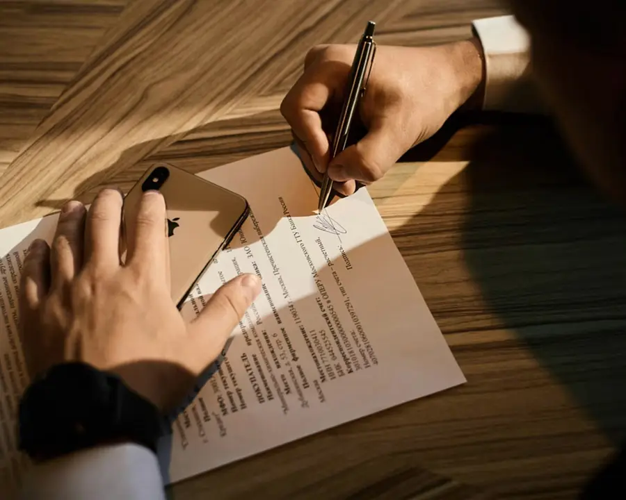 Hands signing an engagement agreement on a wooden desk