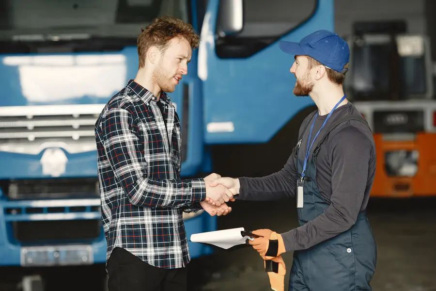 Driver and mechanic shaking hands in front of a truck
